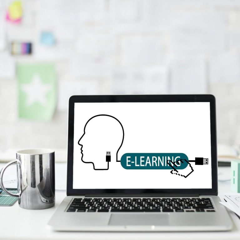 E-Learning Voiceover Services, Birmingham, Alabama A laptop computer sitting on a desk next to a coffee mug, with "e-learning" text on the screen to represent e-learning voiceover services.